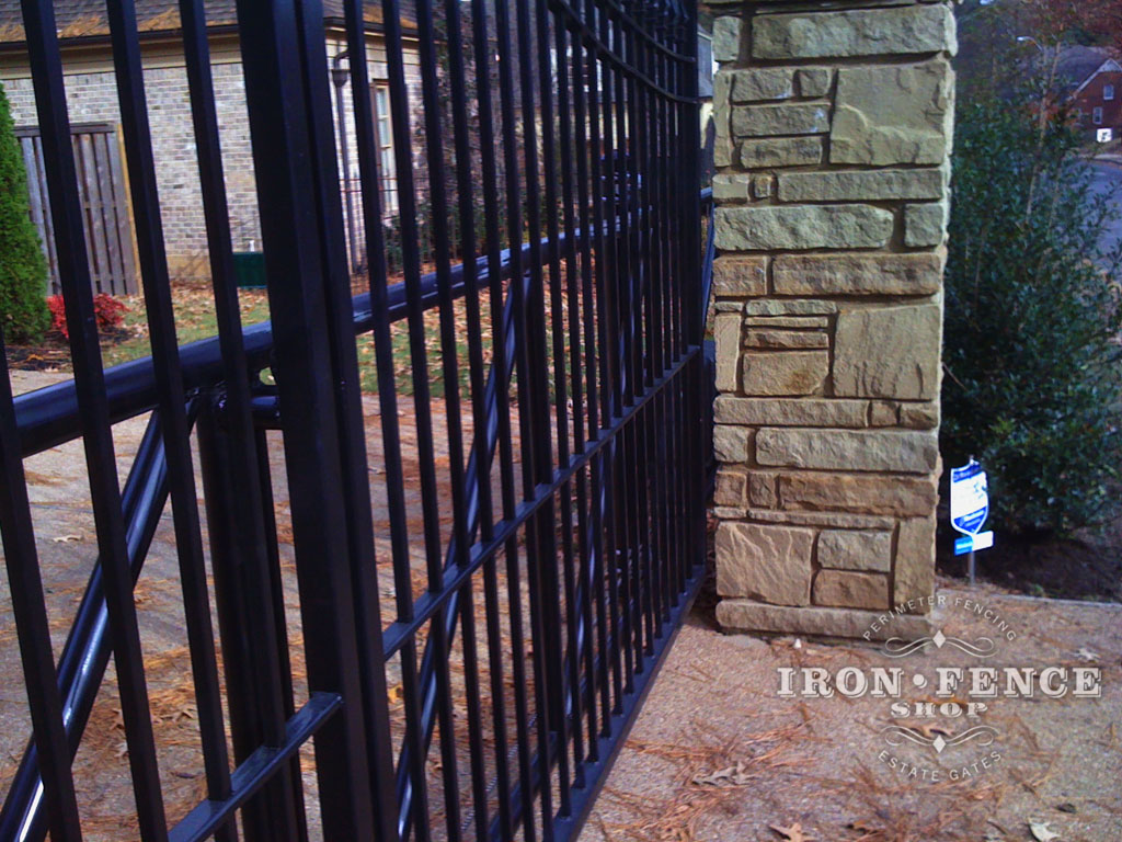 black iron sliding gate installed next to stone pillar