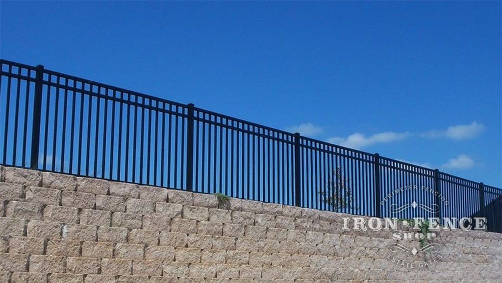 black iron fence installed on stone wall under blue sky